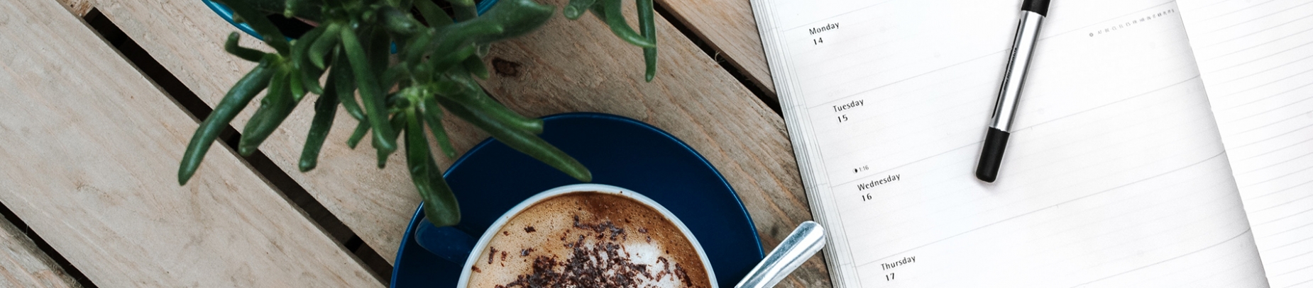 An open diary and pen next to a cup of coffee and a plant